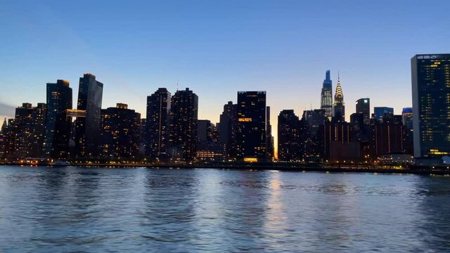 Beautiful shot of New York city seen from the Hudson River with city lights of buildings on a blue sunset