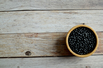 Top Views of Dried Black Beans in a wooden bowl isolated on the wooden background, Full depth of field.