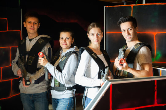 Group portrait of young people with laser guns having fun on dark lasertag arena..