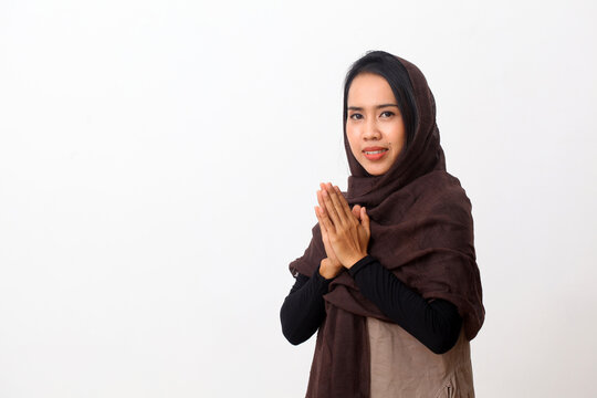 Asian woman in Muslim dress stands up in a greeting pose to Namaste hands, welcoming guests, Eid Fitr greeting. Isolated on white background