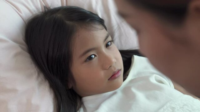 Asian mother checking temperature of sickness little daughter on the bed. Mom caring illness child girl kid by put fever patch on child girl kid forehead. Family and medical health insurance concept