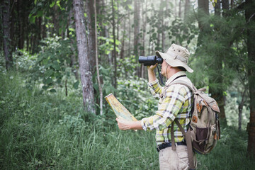 Hiker holding a binoculars and checks map to find directions in wilderness area