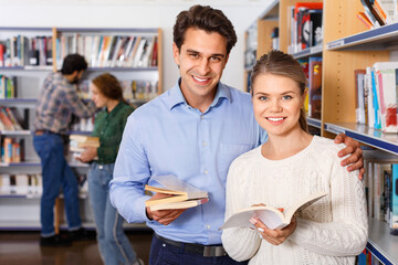 Young happy cheerful positive handsome man and attractive girl choosing books together in university library