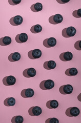 Pattern of blueberry with sunny shadows on pastel pink background. Summer food, organic seasonal berry. Top view, flat lay, vertical