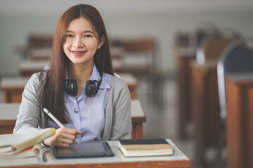 Stock photo of a young teenage woman Asian college student in student uniform studying and writing on a notebook in a university classroom