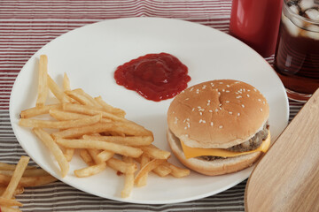 Close-up shot: Ketchup poured into  white empty dish placed on a tablecloth. To eat with junk food placed next to it, such as French fries, hamburgers, and cola, which are unhealthy fast foods.