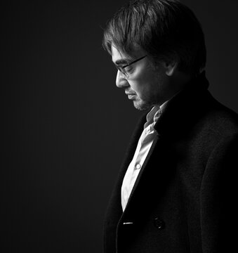 Black And White Profile Of Adult Man In White Shirt And Teed Jacket On Shoulders, Standing Looking Down, Feeling Sad And Sorrow Over Black Background