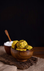 Homemade baked chickpea burgers with white yogurt sauce in brown wooden bowl on burlap cloth on black background. Tasty vegetarian lentils cutlets with greens and spice. Vertical image. Copy space