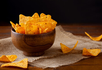 Nachos in brown wooden bowl on burlap cloth on table. Traditional mexican corn chips with spices.