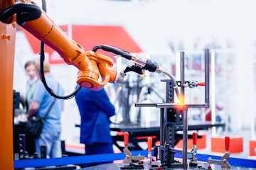 Yellow robot hand performs welding work on metal structures industrial automatic factory, light...