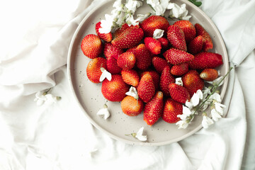 fresh strawberries on plate and small white flowers as decor. healthy food. raw food diet. food content. seasonal berries. selective focus