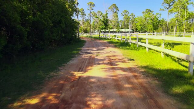 A drone flying along a path leading up to a beutiful horse ranch with white picket fences