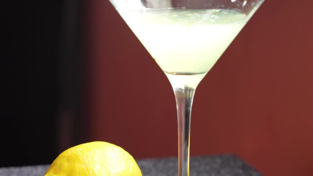 Beautiful Cocktail Shot of Drink in Martini Glass with Lemons, Cucumber Slices and Mint Sprig on the side. Closeup Slow Pan up of Fancy, High-Class Mixed Alcoholic Beverage of Green Color