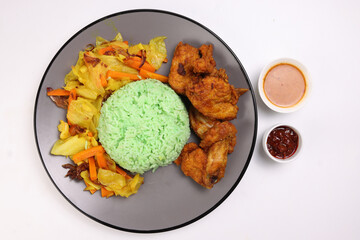 Steamed green rice spiced deep fried chicken cabbage carrot vegetable warung nasi ayam goreng on dark grey plate white background gravy sambal sauce