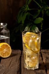 Cold lemonade with lemon and ice in steamed glass on wooden table. Rustic style.