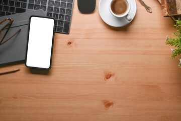 Overhead shot of mock up mobile phone, coffee cup, keyboard and notebook on wooden desk.