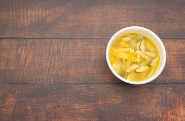 Right frame, soft tom yum soup with omelet, mushroom, galangal, lemongrass in white bowl on wood table