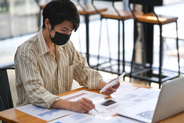Businessman in face mask concentrate analyzing financial data at office desk.