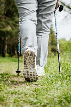 Woman walking in nature. Close-up of boots, trekking poles for outdoor Nordic walking. Active lifestyle. Selective focus on the sole. Vertical photo.