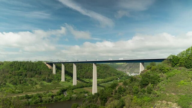 Time lapse shot of traffic on Moselle Bridge during sunny and cloudy day surrounded by green forest trees. Winningen,Germany