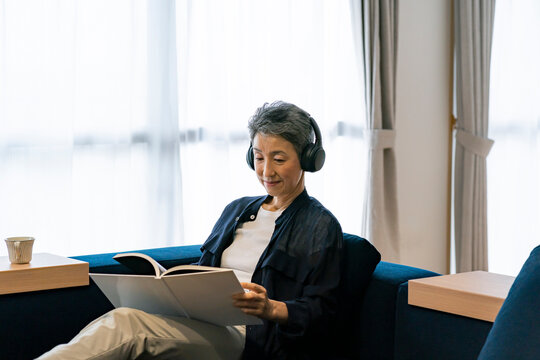 ヘッドホンをして読書をする日本人シニア女性