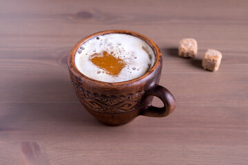 Close-up of hot coffee with milk in a fired earthenware mug with cane sugar pieces. Natural wood background.