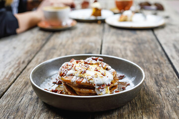 American pancakes with nuts, maple syrup and coconut cream on wooden table. Tasty sweet food for breakfast, brunch or lunch in outdoor cafe or restaurant