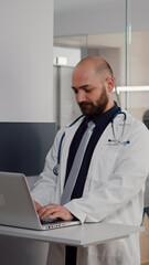 Close up of surgeon doctor wearing medical uniform typing recovery treatment on laptop for sick woman in hospital ward. Black asisstant with hospitalized patient after surgery getting health care