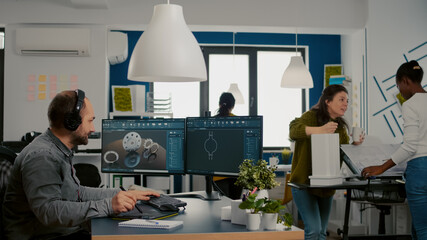 Industrial designer with headset working on PC, screen showing CAD software with 3D construction...