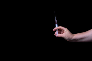 Dark background. a human hand holds a syringe with a dark liquid in it. Close-up.