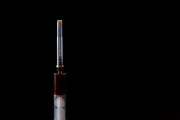 Dark background. the syringe has a dark liquid in it. Concept of drug use Close-up.