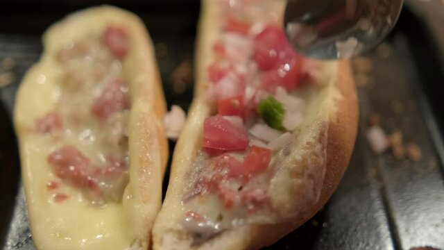 Spoon adding pico de gallo to traditional Mexican molletes above black tray