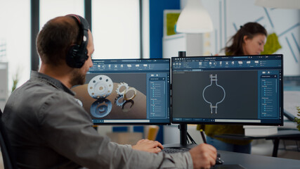 Designer engineer putting on headphones working with technical cad program, analysing 3D gears prototypes, drawing with stylus pencil. Industrial architect studying prototype idea on computer