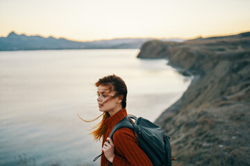 Fototapeta na wymiar beautiful woman in a sweater with a backpack in the mountains near the sea and high rocks sunset nature