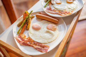 Breakfast with fried eggs, sausage and bacon and vegetables on a white plate.