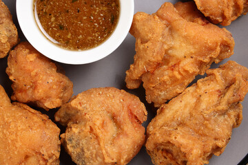 Light battered deep fried chicken variety mix pieces pile flaky meat on grey plate honey garlic clear sauce in center over wooden background