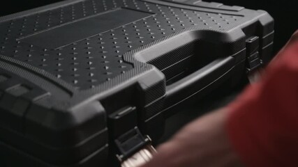 male hands of worker with red sleeves open toolkit black case with chrome vanadium tools