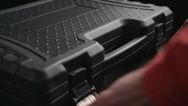 male hands of worker with red sleeves open toolkit black case with chrome vanadium tools
