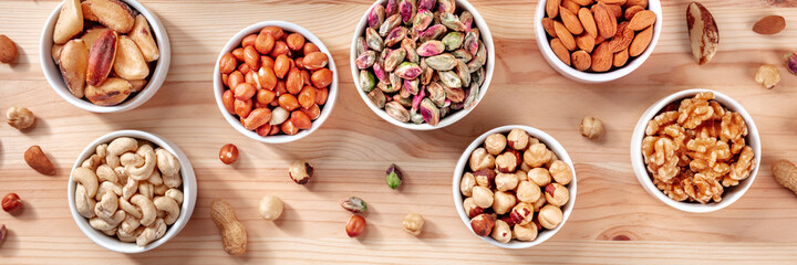 Nuts panorama. Pistachios, peanuts, walnuts and many other nuts, shot from the top on a rustic wooden background