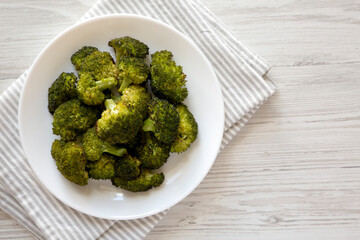 Homemade Roasted Broccoli with Salt and Pepper on a plate on a white wooden background, top view. Flat lay, overhead, from above. Copy space.