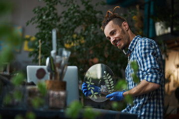 Joyful male herbalist holding glass herbarium and using laptop