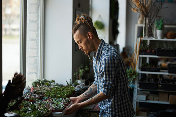 Handsome young man checking plants on windowsill
