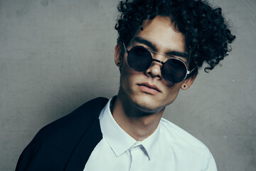 Fototapeta premium portrait of a curly-haired guy in a shirt with a jacket on his shoulder and glasses on his face close-up 