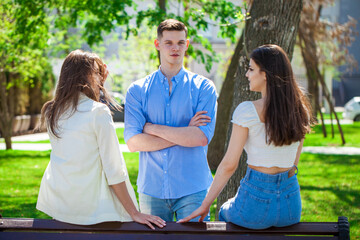 One young guy talking to two girlfriends in a summer park