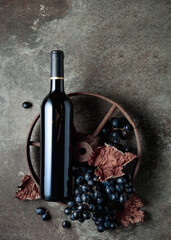 Bottle of red wine with grapes and dried vine leaves on an old stone background.