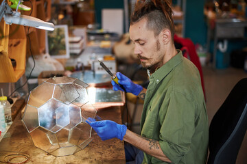 Handsome young man making glass florarium in workshop