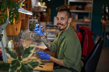Cheerful young man making glass terrarium in workshop