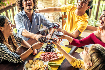 Happy adult friends dining drinking red wine on terrace rooftop home party - Multiracial young people at lunch having fun eating bbq food in gastronomic rustic restaurant - Friendship, youth concept