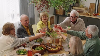 High angle view of company of senior friends sitting together at dinner table, smiling and clinking wine glasses in toast - Powered by Adobe