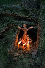 magic witchcraft doll made of tree bast and burning candles in dark forest. Forest grandmother,...